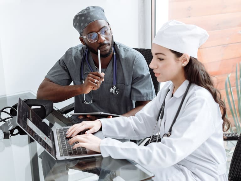 Médecin et collègue en blouse blanche échangeant sur un dossier devant un ordinateur portable