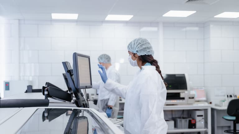 Technologue en tenue de protection utilisant l'écran tactile d'un analyseur clinique automatisé