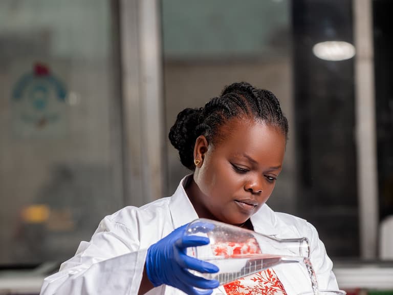 Scientifique de laboratoire en blouse et gants transvasant un liquide, à Kinshasa